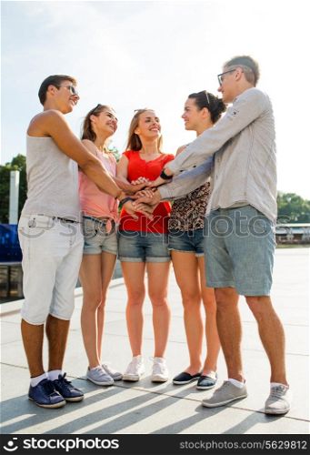 friendship, leisure, summer, gesturer and people concept - group of smiling friends with hands on top in city