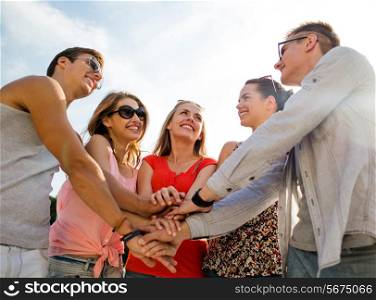 friendship, leisure, summer, gesturer and people concept - group of smiling friends with hands on top in city