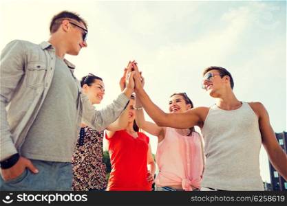 friendship, leisure, summer, gesturer and people concept - group of smiling friends making high five outdoors