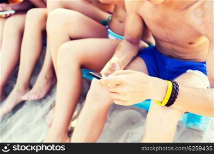 friendship, leisure, summer, technology and people concept - close up of friends with smartphones sitting on sandy beach