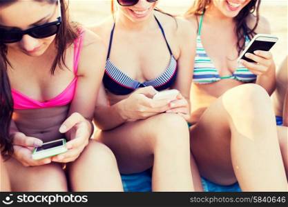friendship, leisure, summer, technology and people concept - close up of smiling friends with smartphones sitting on sandy beach