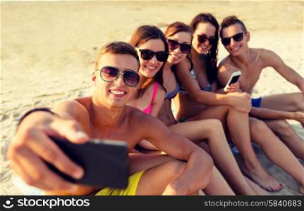friendship, leisure, summer, technology and people concept - friends sitting and taking selfie with smartphone on beach