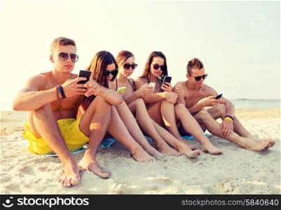 friendship, leisure, summer, technology and people concept - group of friends with smartphones sitting on beach