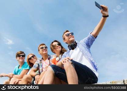 friendship, leisure, summer, technology and people concept - group of happy friends with smartphone taking selfie outdoors