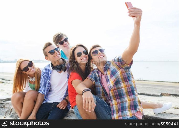 friendship, leisure, summer, technology and people concept - group of happy friends with smartphone taking selfie outdoors