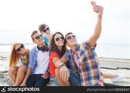 friendship, leisure, summer, technology and people concept - group of happy friends with smartphone taking selfie outdoors