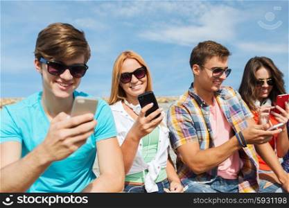 friendship, leisure, summer, technology and people concept - group of happy friends with smartphones outdoors