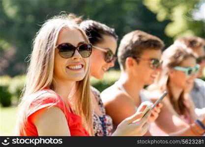 friendship, leisure, summer, technology and people concept - group of smiling friends with smartphones sitting in park