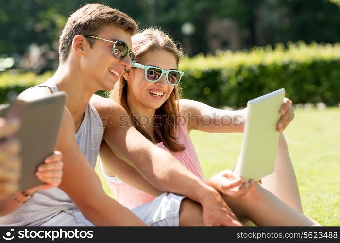 friendship, leisure, summer, technology and people concept - group of smiling friends with tablet pc computers sitting on grass in park