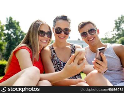 friendship, leisure, summer, technology and people concept - group of smiling friends with smartphone sitting on grass and making selfie in park
