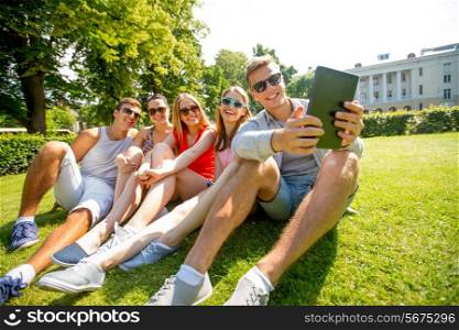 friendship, leisure, summer, technology and people concept - group of smiling friends with tablet pc computer sitting and making selfie in park