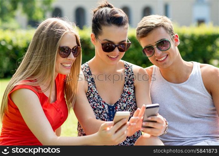 friendship, leisure, summer, technology and people concept - group of smiling friends with smartphone sitting on grass in park