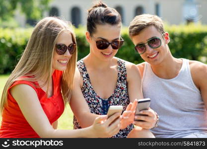 friendship, leisure, summer, technology and people concept - group of smiling friends with smartphone sitting on grass in park