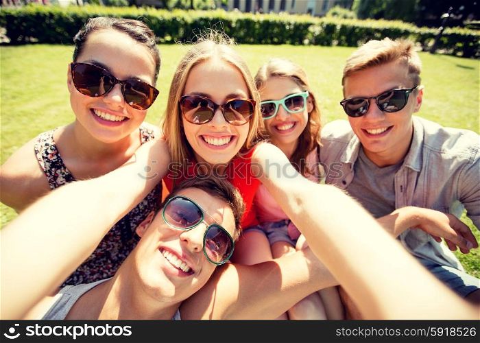 friendship, leisure, summer, technology and people concept - group of smiling friends making selfie with smartphone, camera or tablet pc in park