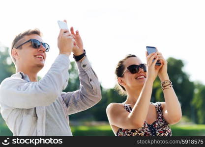 friendship, leisure, summer, technology and people concept - group of smiling friends with smartphone taking picture outdoors