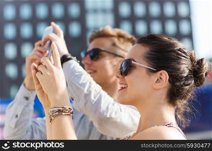 friendship, leisure, summer, technology and people concept - group of smiling friends with smartphone taking picture outdoors