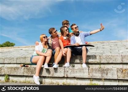 friendship, leisure, summer, technology and people concept - group of smiling friends with skateboard and smartphone taking selfie outdoors