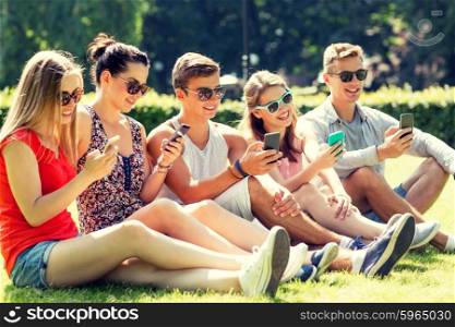 friendship, leisure, summer, technology and people concept - group of smiling friends with smartphones sitting on grass in park