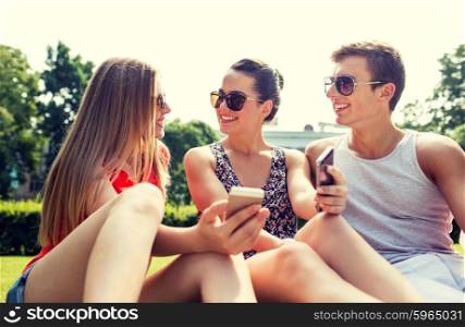 friendship, leisure, summer, technology and people concept - group of smiling friends with smartphones sitting on grass and talking in park