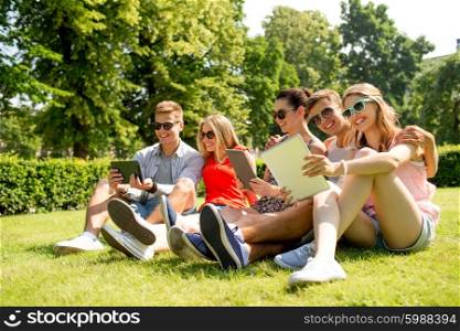 friendship, leisure, summer, technology and people concept - group of smiling friends with tablet pc computers sitting on grass in park