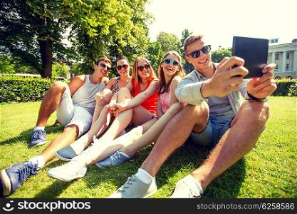 friendship, leisure, summer, technology and people concept - group of smiling friends with tablet pc computer sitting and making selfie in park