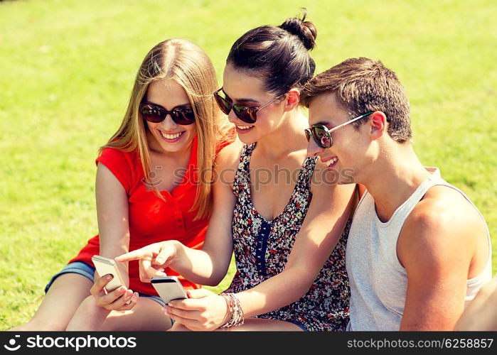 friendship, leisure, summer, technology and people concept - group of smiling friends with smartphones sitting on grass in park