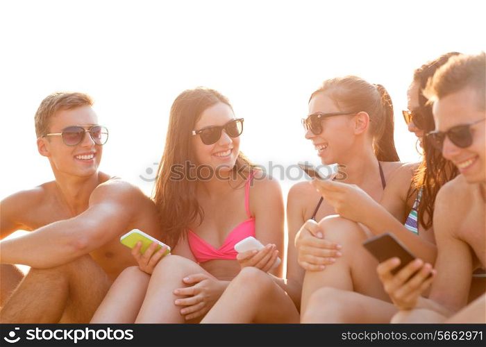 friendship, leisure, summer, technology and people concept - group of smiling friends with smartphones on beach