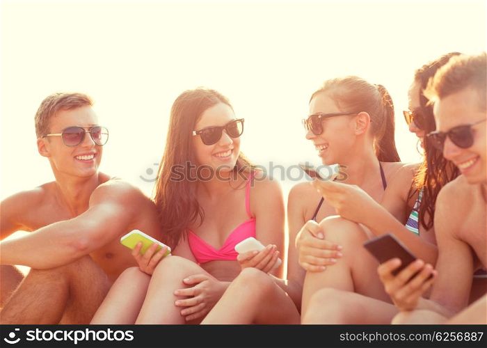 friendship, leisure, summer, technology and people concept - group of smiling friends with smartphones on beach