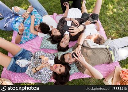 friendship, leisure, technology and people concept - group of friends with smartphones chilling on picnic blanket at summer park. friends with smartphones on picnic blanket. friends with smartphones on picnic blanket