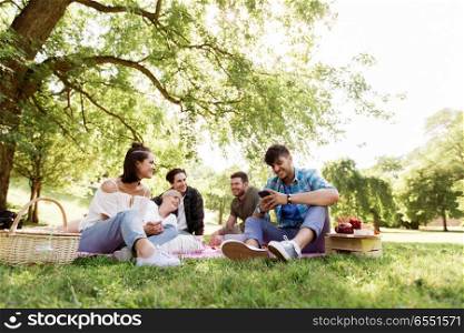 friendship, leisure, technology and people concept - group of friends with smartphones chilling on picnic blanket at summer park. friends with smartphones on picnic at summer park. friends with smartphones on picnic at summer park