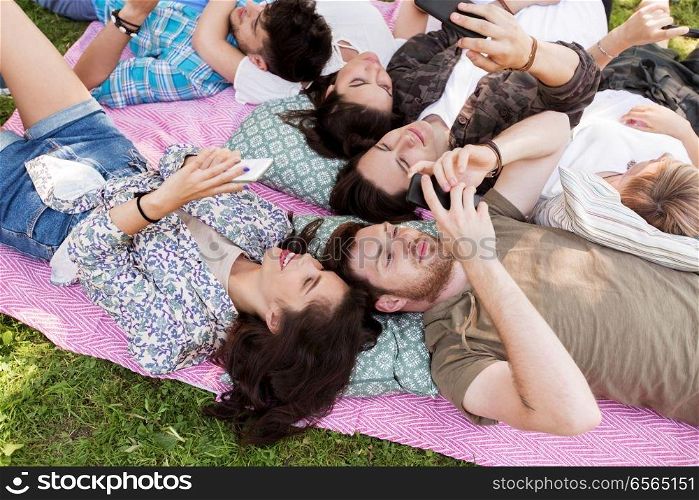 friendship, leisure, technology and people concept - group of friends with smartphones chilling on picnic blanket at summer park. friends with smartphones on picnic blanket