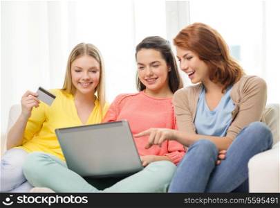 friendship, money, technology and internet concept - three smiling teenage girls with laptop computer and credit card at home