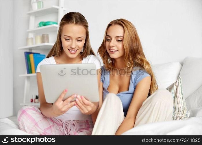 friendship, pajama party and technology concept - happy friends or teenage girls with tablet pc computer at home. happy friends or teen girls with tablet pc at home