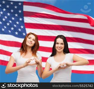 friendship, patriotic and happy people concept - two smiling girls in white blank t-shirts showing heart with hands