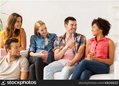 friendship, people and entertainment concept - happy friends with popcorn and beer talking at home