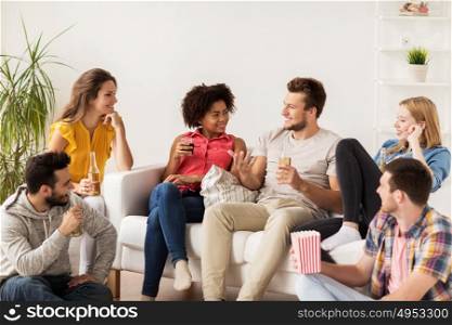 friendship, people and entertainment concept - happy friends with popcorn and beer talking at home. happy friends with popcorn and beer at home