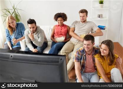 friendship, people and entertainment concept - happy friends with popcorn and beer watching tv at home. happy friends with popcorn watching tv at home
