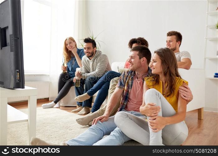 friendship, people and entertainment concept - happy friends with popcorn and beer watching tv at home. happy friends with popcorn watching tv at home