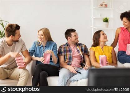 friendship, people and entertainment concept - happy friends with popcorn and tv remote talking at home. happy friends with popcorn and tv remote at home