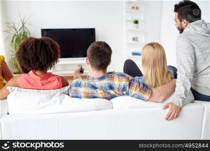 friendship, people and entertainment concept - happy friends with remote watching tv at home. happy friends with remote watching tv at home