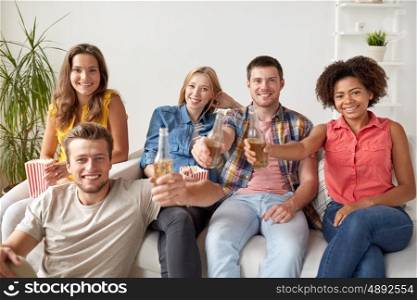 friendship, people and holidays concept - happy friends with popcorn drinking beer at home