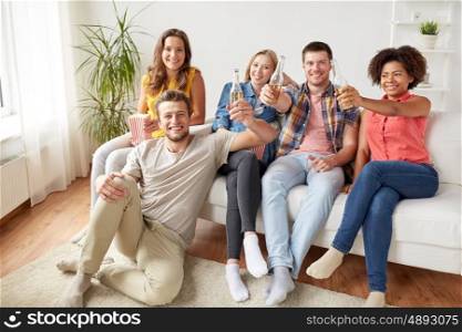 friendship, people and holidays concept - happy friends with popcorn drinking beer at home
