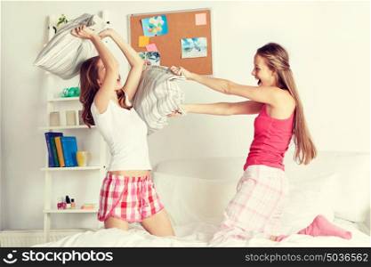 friendship, people and pajama party concept - happy friends or teenage girls having fun and pillow fight on bed at home. happy teen girl friends fighting pillows at home