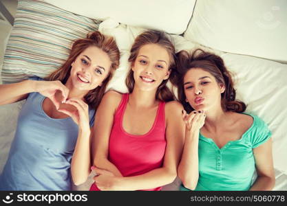 friendship, people and pajama party concept - happy friends or teenage girls having fun and lying in bed at home. happy young women in bed at home pajama party