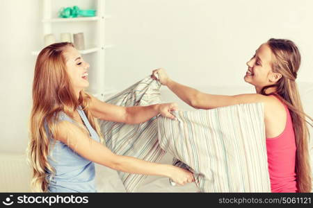 friendship, people and pajama party concept - happy friends or teenage girls having fun and pillow fight on bed at home. happy teen girl friends fighting pillows at home