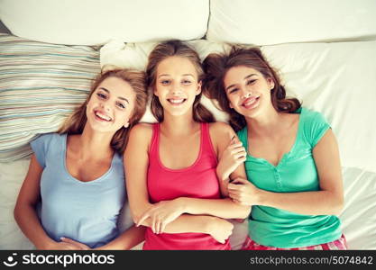 friendship, people and pajama party concept - happy friends or teenage girls having fun and lying in bed at home. happy young women in bed at home pajama party