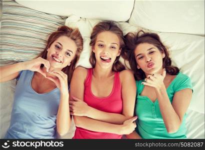 friendship, people and pajama party concept - happy friends or teenage girls having fun and lying in bed at home. happy young women in bed at home pajama party