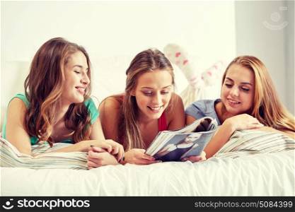 friendship, people and pajama party concept - happy friends or teenage girls reading magazine in bed at home. friends or teen girls reading magazine at home. friends or teen girls reading magazine at home