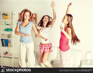friendship, people and pajama party concept - happy friends or teenage girls having fun, dancing and jumping on bed at home. happy friends or teen girls having fun at home