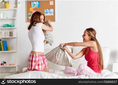 friendship, people and pajama party concept - happy friends or teenage girls having fun and pillow fight on bed at home